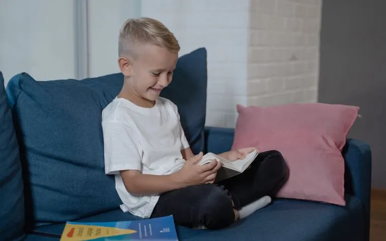 Enfant souriant qui lit un livre sur le canapé